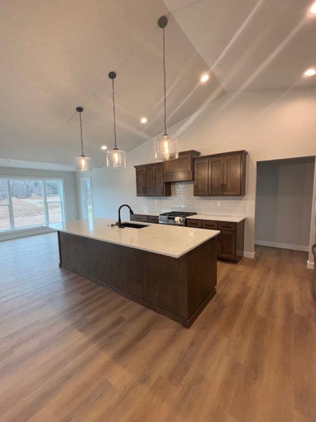 kitchen with stainless steel gas range oven, an island with sink, a sink, wood finished floors, and dark brown cabinets