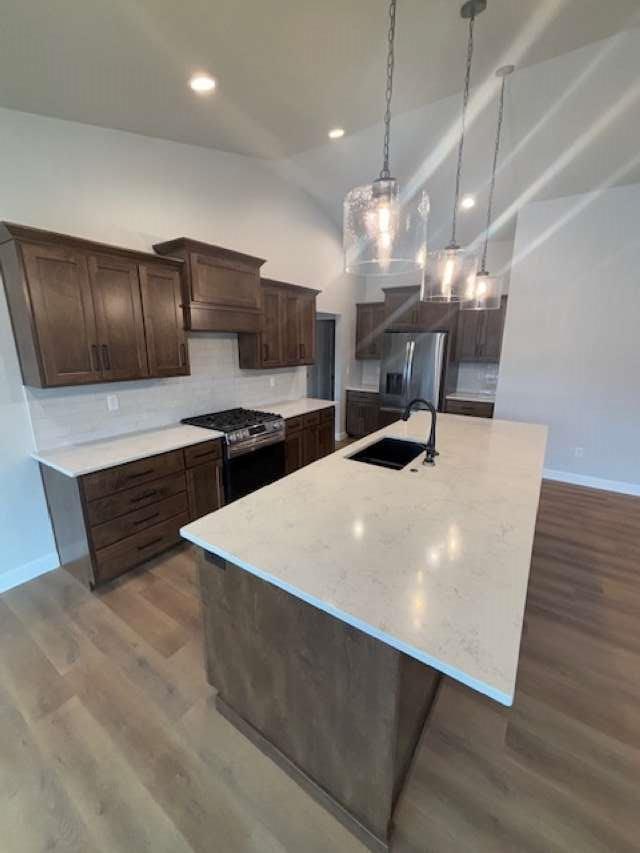 kitchen with a large island, a sink, dark wood-style floors, appliances with stainless steel finishes, and dark brown cabinets