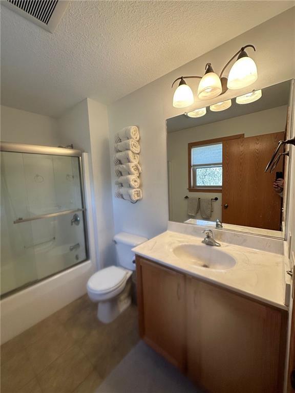 bathroom with visible vents, toilet, a textured ceiling, bath / shower combo with glass door, and vanity