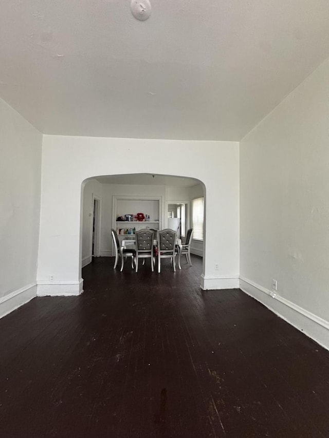 unfurnished dining area featuring arched walkways, baseboards, and wood finished floors