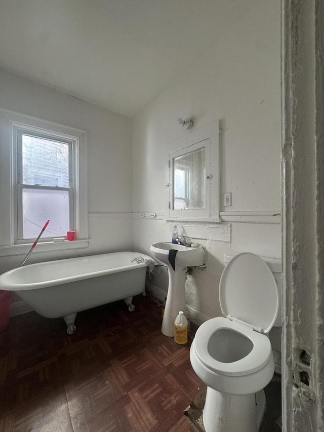 full bath featuring lofted ceiling, a freestanding tub, toilet, and wainscoting