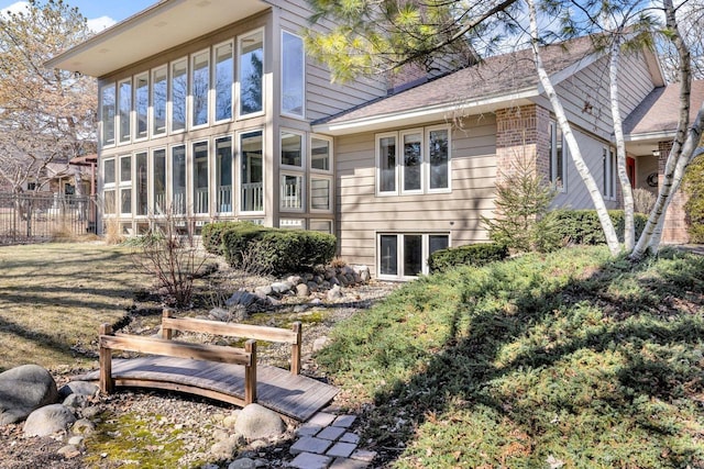 back of house with fence, a sunroom, and a shingled roof