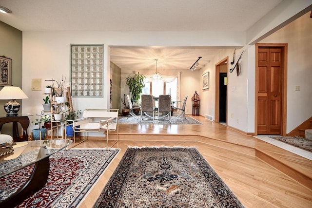 living room featuring a chandelier, visible vents, baseboards, and wood finished floors