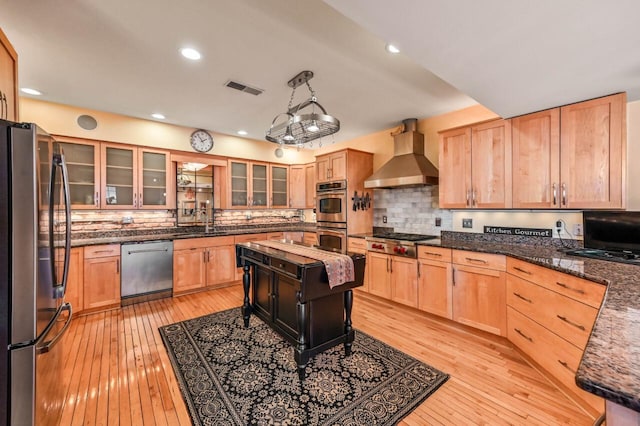 kitchen featuring visible vents, stainless steel appliances, dark stone counters, wall chimney exhaust hood, and light wood finished floors