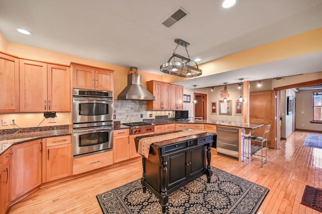 kitchen with visible vents, a peninsula, light wood-style floors, appliances with stainless steel finishes, and wall chimney range hood