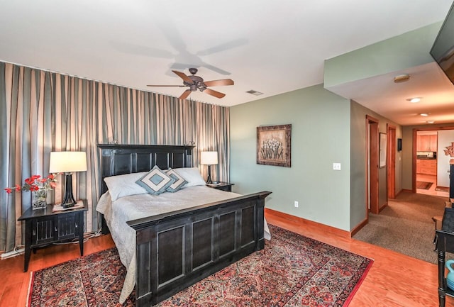 bedroom featuring visible vents, a ceiling fan, wood finished floors, wallpapered walls, and baseboards