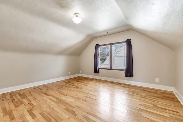 bonus room with baseboards, light wood-style floors, vaulted ceiling, and a textured ceiling