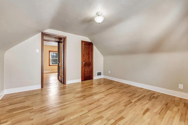 additional living space featuring visible vents, light wood-style floors, baseboards, and lofted ceiling