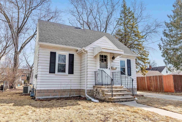 bungalow-style house with cooling unit, roof with shingles, and fence