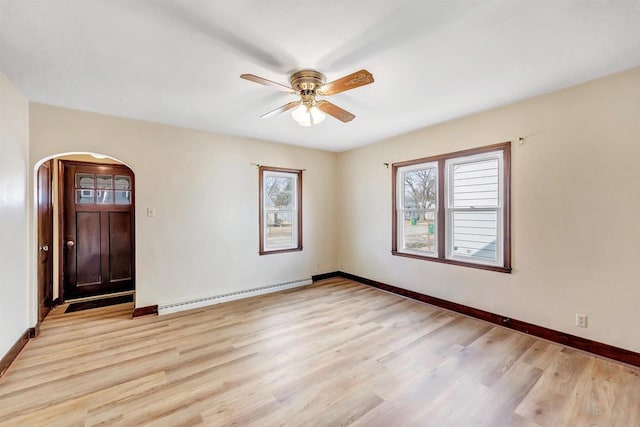 empty room with a ceiling fan, a baseboard heating unit, arched walkways, light wood-style floors, and baseboards