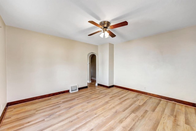 empty room featuring baseboards, visible vents, arched walkways, ceiling fan, and light wood-type flooring