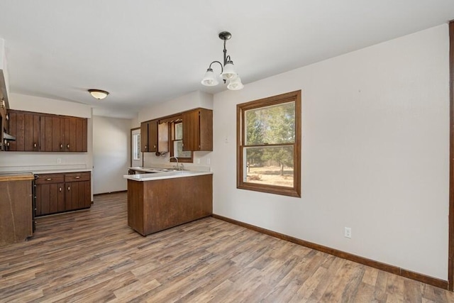 kitchen with baseboards, light countertops, a peninsula, wood finished floors, and a notable chandelier