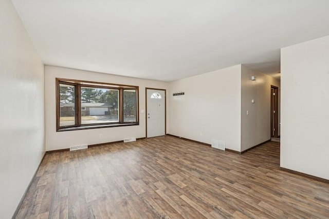 empty room featuring wood finished floors, visible vents, and baseboards