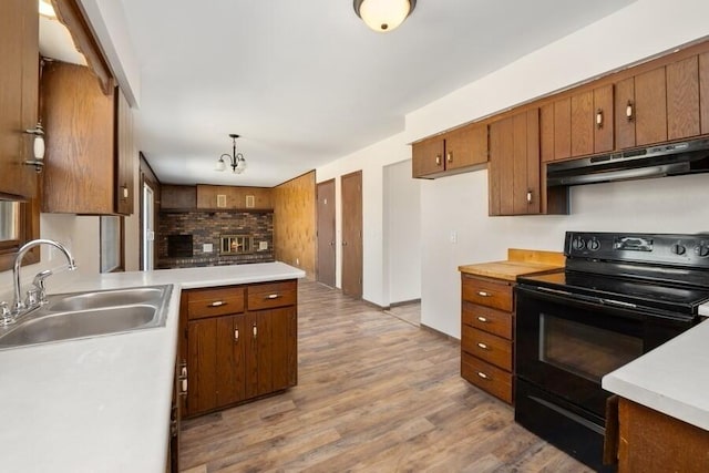 kitchen featuring black / electric stove, brown cabinetry, a sink, light countertops, and under cabinet range hood