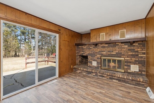 unfurnished living room featuring wooden walls, light wood-style flooring, a fireplace, and visible vents