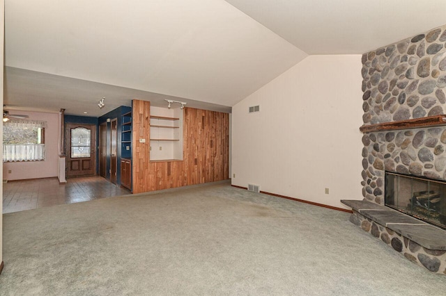 unfurnished living room featuring a stone fireplace, lofted ceiling, carpet flooring, and visible vents