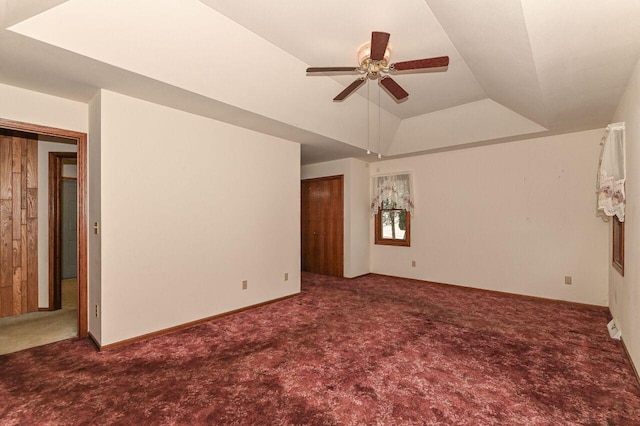 carpeted empty room with a raised ceiling, baseboards, and ceiling fan