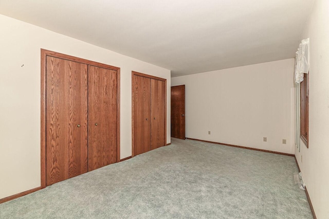 unfurnished bedroom featuring baseboards, multiple closets, and carpet flooring