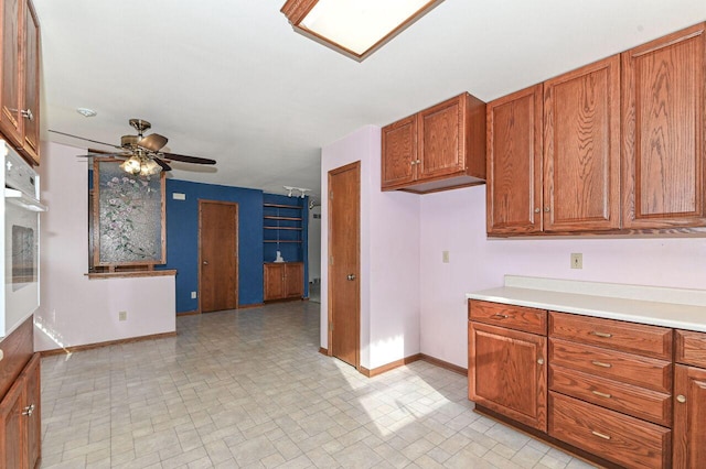 kitchen featuring baseboards, ceiling fan, light countertops, brown cabinetry, and white oven