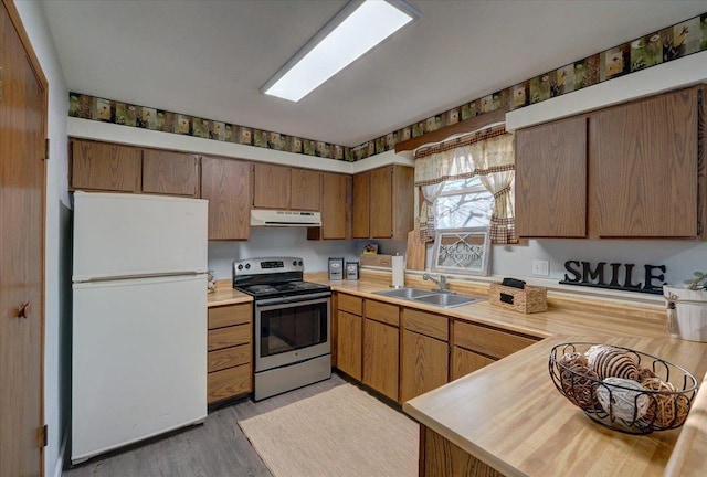 kitchen featuring electric range, a sink, under cabinet range hood, freestanding refrigerator, and light countertops