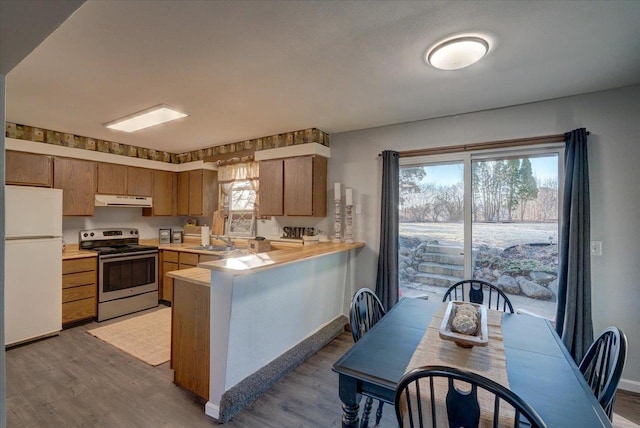 kitchen with under cabinet range hood, freestanding refrigerator, stainless steel range with electric cooktop, a peninsula, and light countertops