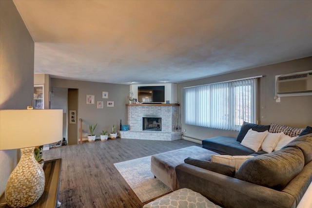 living area with a fireplace, a wall unit AC, wood finished floors, and a baseboard heating unit