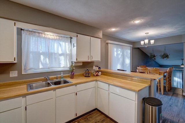 kitchen featuring a sink, dark wood-style floors, a peninsula, white cabinets, and a chandelier