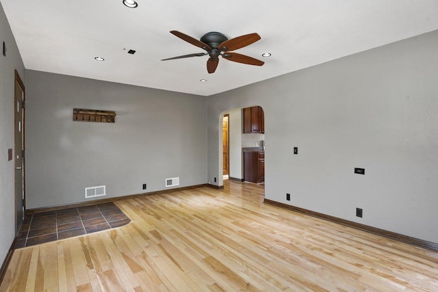 unfurnished room featuring arched walkways, visible vents, light wood-style floors, and a ceiling fan