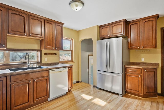 kitchen featuring a sink, dark countertops, freestanding refrigerator, arched walkways, and white dishwasher