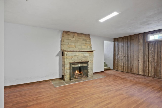 unfurnished living room with stairway, wood walls, a fireplace, and wood finished floors