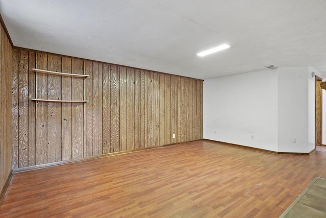 spare room featuring visible vents, baseboards, wooden walls, and wood finished floors