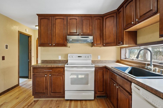 kitchen featuring baseboards, under cabinet range hood, light wood-style floors, white appliances, and a sink