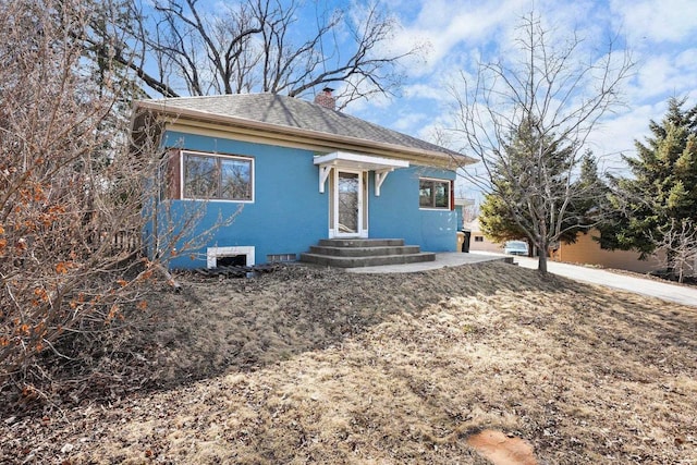 bungalow-style house featuring stucco siding, entry steps, a chimney, and roof with shingles