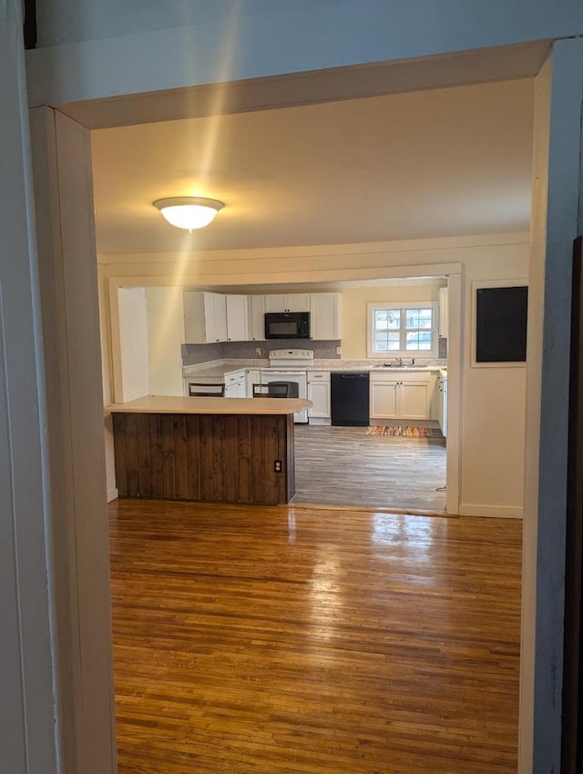 kitchen featuring wood finished floors, a peninsula, black appliances, white cabinets, and light countertops