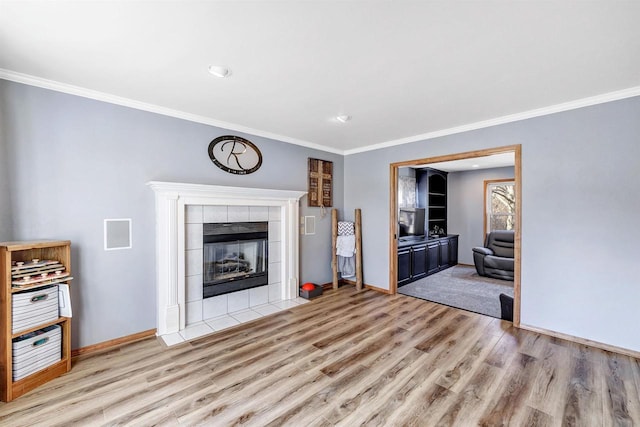 unfurnished living room with a tiled fireplace, ornamental molding, baseboards, and wood finished floors