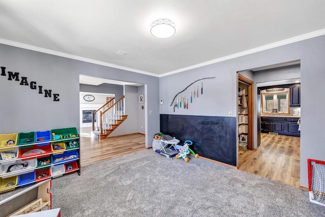 recreation room featuring carpet flooring, wood finished floors, and ornamental molding