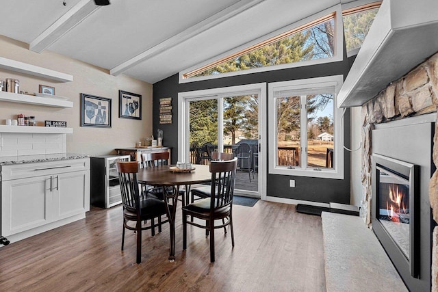 dining room with a glass covered fireplace, wine cooler, vaulted ceiling with beams, and wood finished floors