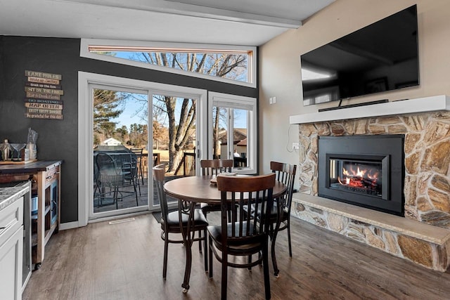 dining area featuring a stone fireplace, beam ceiling, wood finished floors, and baseboards