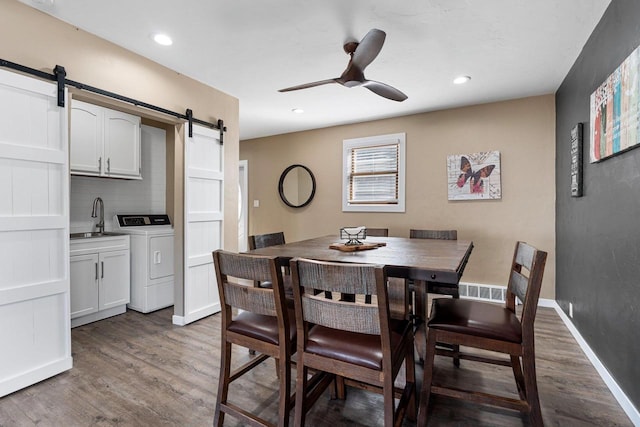 dining area featuring wood finished floors, baseboards, ceiling fan, a barn door, and washing machine and dryer