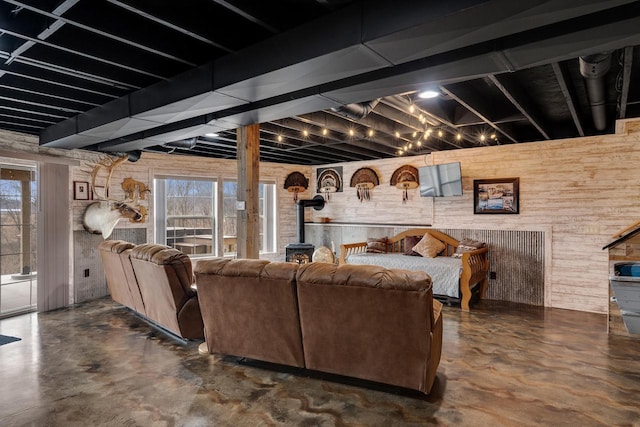 living area with a wealth of natural light, wooden walls, finished concrete flooring, and a wood stove