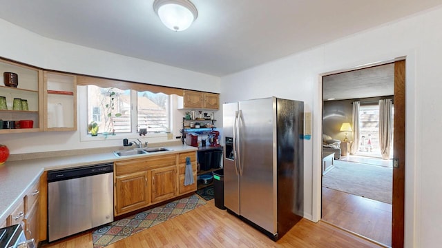 kitchen with light wood-type flooring, a sink, light countertops, appliances with stainless steel finishes, and brown cabinets