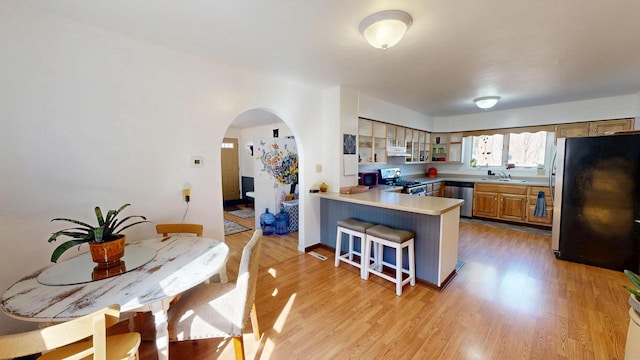 kitchen with a breakfast bar, light wood-type flooring, a peninsula, arched walkways, and stainless steel appliances