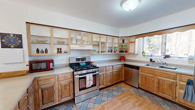 kitchen with light wood-style flooring, under cabinet range hood, a sink, appliances with stainless steel finishes, and light countertops