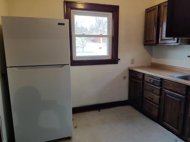 kitchen featuring a sink, freestanding refrigerator, dark brown cabinetry, light countertops, and baseboards