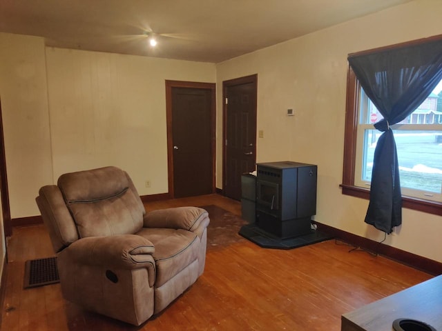 sitting room featuring a wood stove, wood finished floors, visible vents, and baseboards