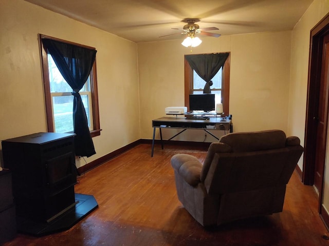 office space featuring a ceiling fan, a wood stove, wood finished floors, and baseboards