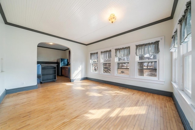 unfurnished living room with arched walkways, baseboards, crown molding, and light wood-style floors