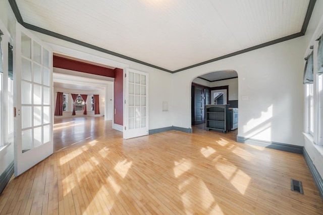 empty room with arched walkways, visible vents, crown molding, and light wood-type flooring