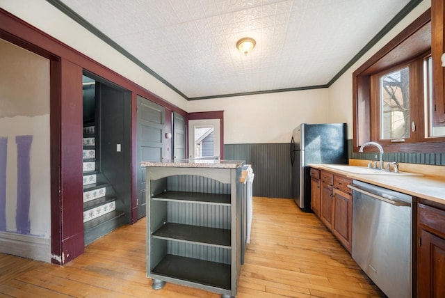 kitchen with a wainscoted wall, light countertops, ornamental molding, light wood-style flooring, and appliances with stainless steel finishes