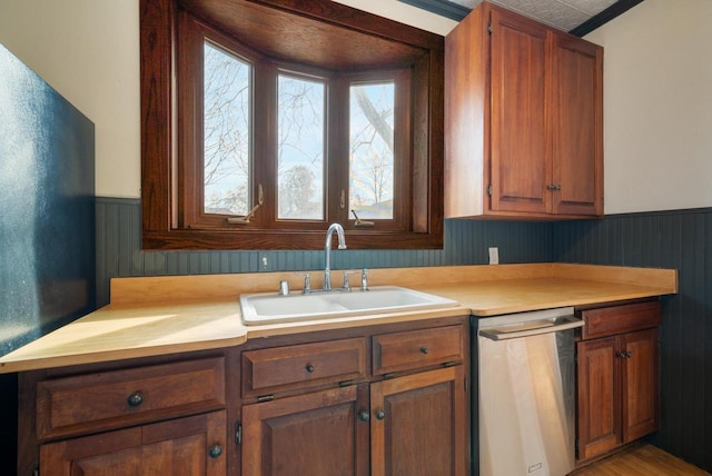 kitchen with a sink, light countertops, a wainscoted wall, and stainless steel dishwasher